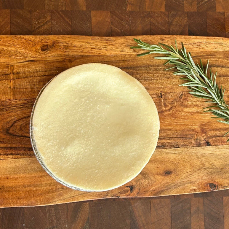 Pie crust on a wooden cutting board with a sprig of rosemary
