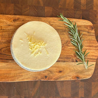 A cheeseburger brisket pie on a wooden cutting board, garnished with a sprig of dill, with cheese visible on top.