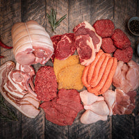 A variety of raw meats arranged on a wooden surface, including steaks, sausages, mince, burger patties, chicken breasts, and bacon.